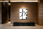 A framed abstract black and white calligraphic art print hangs on a textured brown stone wall above a black marble console table in a modern interior setting.