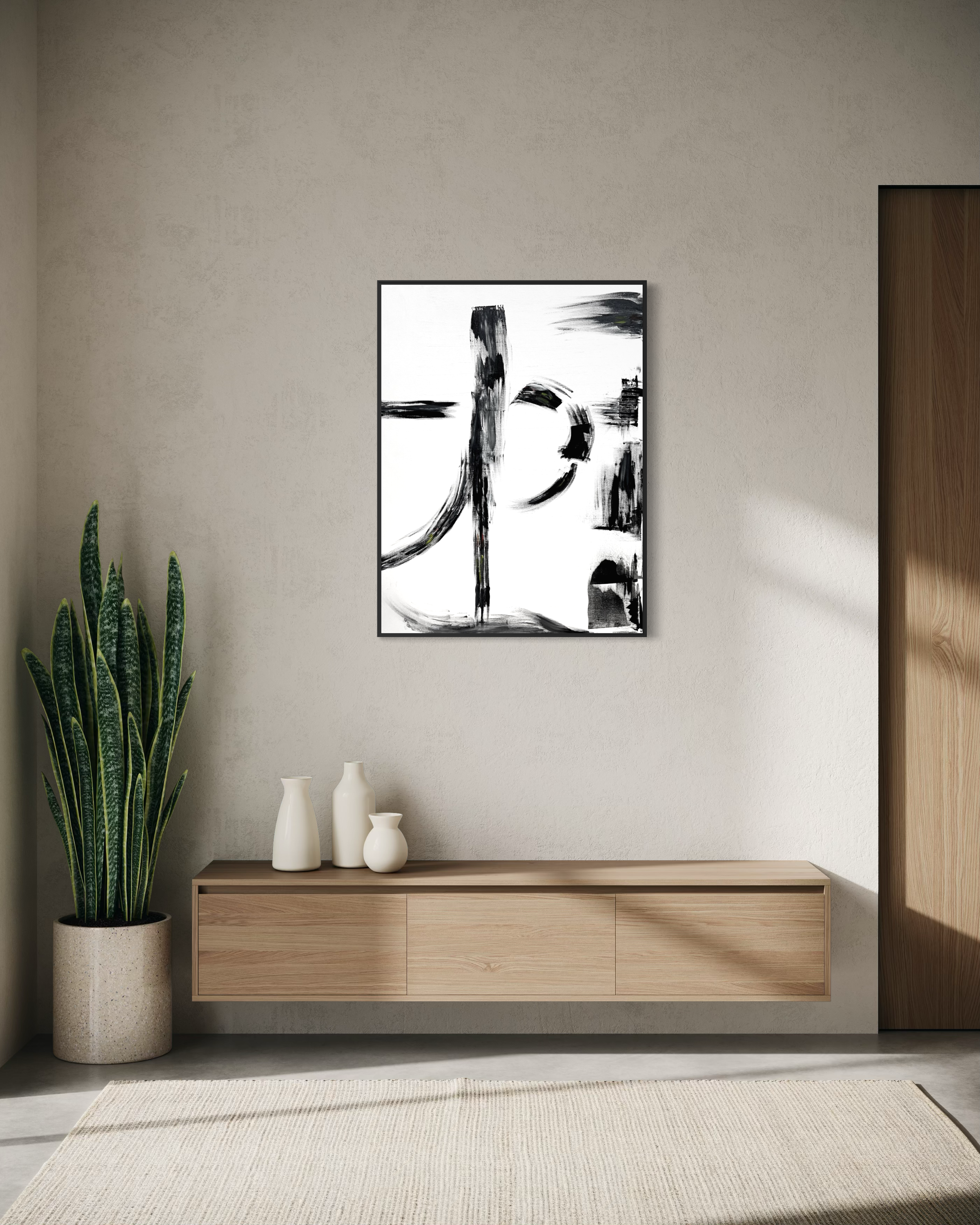 A framed abstract black and white calligraphic wall art print hangs on a textured beige wall above a light wood console table with ceramic vases, next to a potted snake plant.