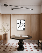 A modern interior room with light wood paneled walls, a round black table, a black pendant light, and a framed black-and-white abstract artwork centered on the wall.
