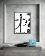 A framed abstract black and white painting is displayed on a textured gray wall above a concrete shelf holding books, a turntable, and a blue box.