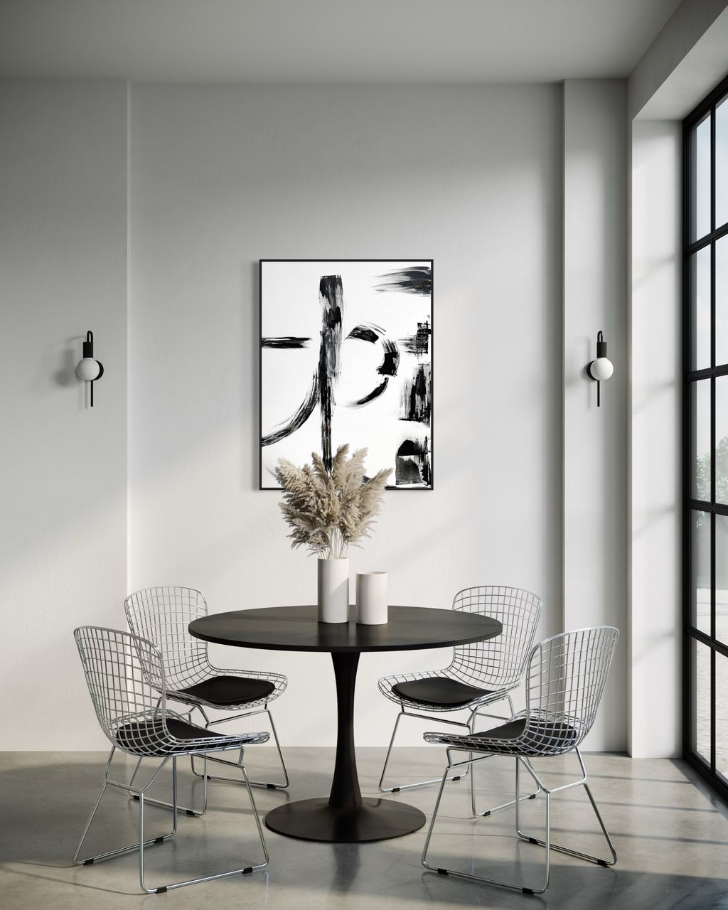 A modern dining room scene with a round black table and four wire-frame chairs, styled with a vase of dried grass and two white candles. On the wall above the table is a large black-and-white abstract art print.